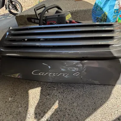 Porsche Carrera 4 rear deck lid and engine cover grill panel with visible denting, shown alongside garden supplies and power tools.