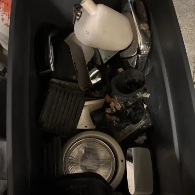 Large grey storage tote filled with various vintage automotive parts, including a headlight, side mirror, reservoir bottle, and chrome...