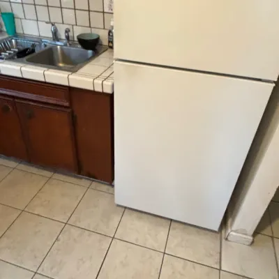 White top-freezer refrigerator in a kitchen setting next to tiled countertops and wooden cabinetry.