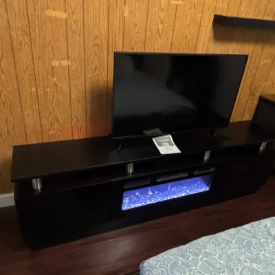 Modern black media console with an integrated electric fireplace insert, supporting a flat-screen television.