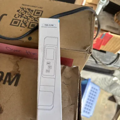 Boxed TDS-5/5B digital water quality test pen resting on cardboard boxes.