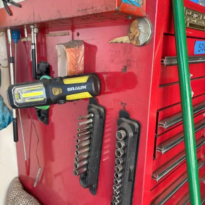 Red metal rolling tool chest equipped with magnetic accessories, including a Braun LED work light and socket organizers.