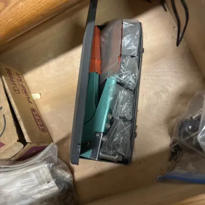 Hand rivet tool kit with assorted rivets in a plastic case, stored in a wooden drawer alongside hardware supplies.