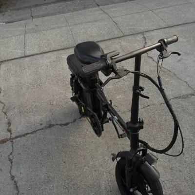 Black Sport-brand compact folding electric bike with a front headlight and padded seat, shown outdoors on concrete pavement.