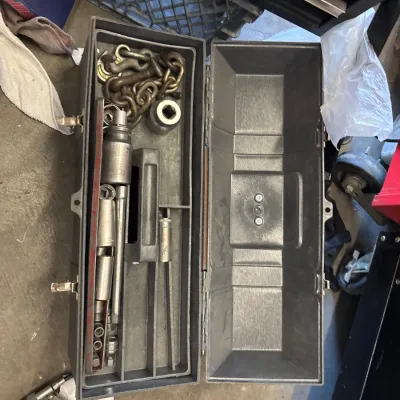 Open metallic grey toolbox filled with various sockets, socket extensions, and a heavy-duty tow chain with hooks.