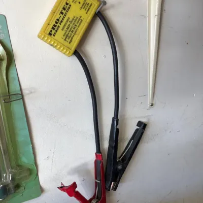 Vintage Pro-Tec 12-volt automotive surge protector unit with red and black terminal clamps, hanging on a garage wall.