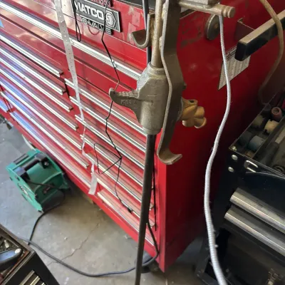 Vintage metal bumper jack mechanism standing upright in front of a red Matco tool chest.