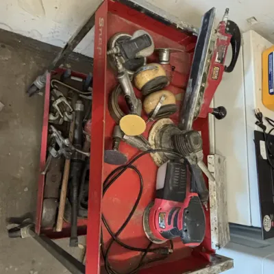 Red metal tool cart filled with various power and pneumatic tools, including orbital sanders and hand tools.