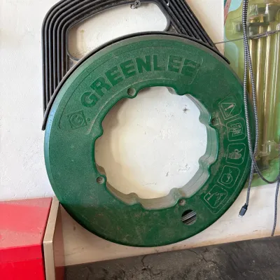 Greenlee steel fish tape reel in a green and black plastic case, showing light cosmetic wear from use.