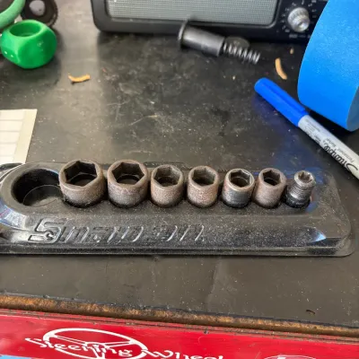 Snap-on plastic socket holder tray organized with various weathered hex sockets on a workshop bench.