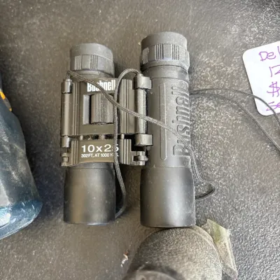 Compact Bushnell 10x25 folding binoculars in black rubber armor with attached neck strap.