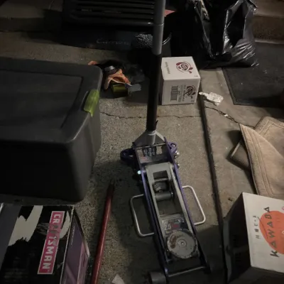 Pittsburgh Racing 2.5-ton aluminum floor jack in purple and silver, surrounded by garage items and storage boxes.