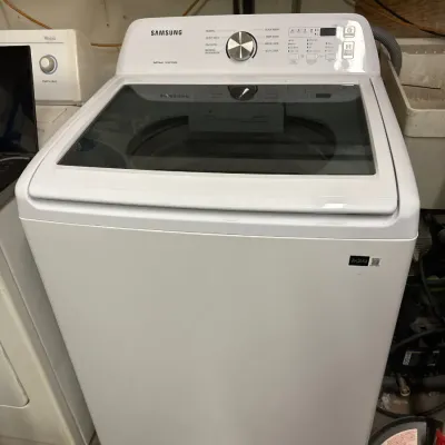 White Samsung top-loading washing machine featuring a glass lid, stainless steel dial selector, and digital control panel.