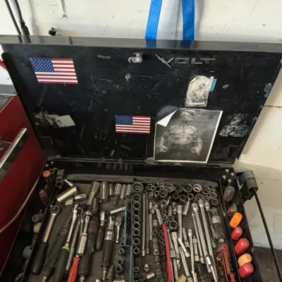 Black Volt mechanic's tool chest loaded with various socket wrenches, extensions, and hand tools. The lid is decorated with stickers...