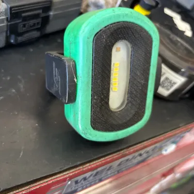 Snap-on portable LED work light with a green rubberized housing and a black mounting clip, showing light wear.