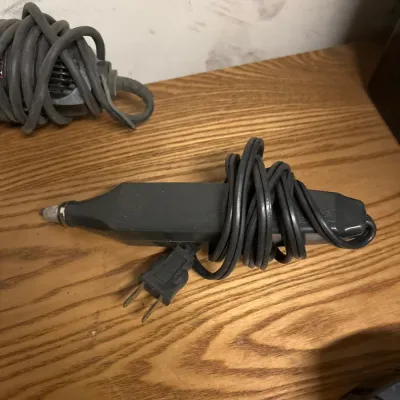 Handheld electric engraving tool with wrapped power cord resting on a wooden surface.