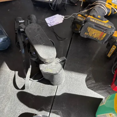 Vintage Sears binoculars with a protective leather neck strap alongside DeWalt power tools on a dark surface.