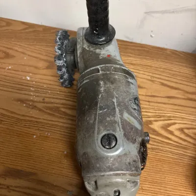 Vintage heavy-duty electric angle grinder with attached wire wheel attachment, showing heavy surface wear from use.