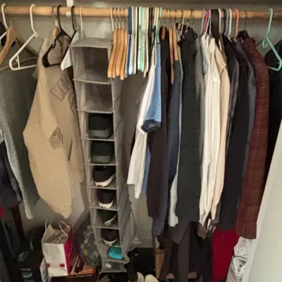 Closet filled with assorted men's and women's clothing, including jackets, shirts, and a hanging fabric shoe organizer.