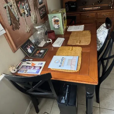 Two-tone wooden dining table with turned black legs and matching x-back chairs, surrounded by household accessories and a large wall-hung...