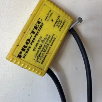 Vintage Pro-Tec 12-volt surge protector unit in a yellow plastic housing, mounted on a wall.