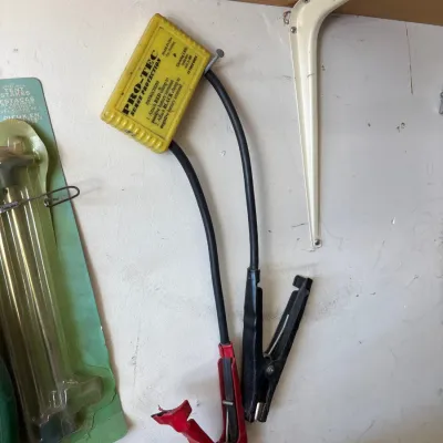 Vintage Pro-Tec yellow 12-volt surge protector with battery terminal clamps, hanging on a workshop wall.
