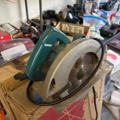 Vintage Makita teal corded circular saw resting on a cardboard box, showing signs of prior use.