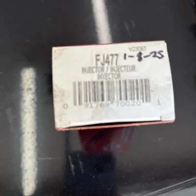 Boxed FJ477 fuel injector with handwritten date label, displayed on a black surface.