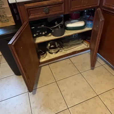 Open wooden kitchen cabinet filled with various cookware, including an Oster toaster, pots, glass baking dishes, and a stainless steel...