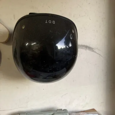 Black DOT-approved open-face motorcycle helmet, hanging on a wall alongside various garage items.