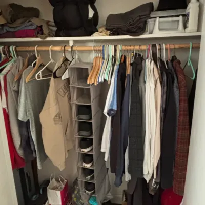 A closet filled with men's clothing, including jackets, shirts, sweaters, and a fabric hanging shoe organizer.