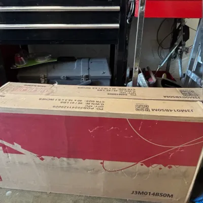 Two large cardboard shipping boxes for flat-packed furniture items, stacked vertically on a garage floor.