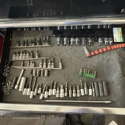 Open tool chest drawer filled with a large collection of assorted socket set attachments, hex bits, Torx drivers, and extension bars in...