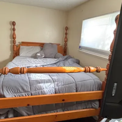 Traditional pine four-poster bed frame featuring turned finial posts, set up with bedding in a bedroom.