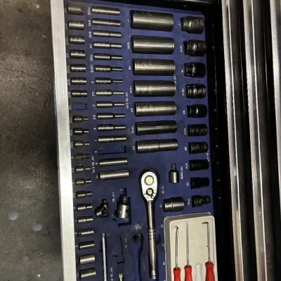 Open tool chest drawer organized with an extensive socket set, ratchet, extension bars, and small pick tools, all resting in custom blue...