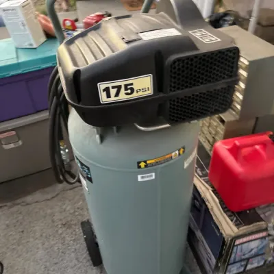Portable vertical air compressor rated at 175 PSI, featuring a wheeled base, top handle, and attached hose.