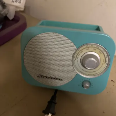 Vintage-style teal Studebaker AM/FM tabletop radio with a silver mesh speaker grill and circular tuning dial.