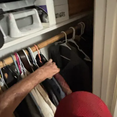 Assorted clothing items hanging on hangers in a closet, alongside top shelves with cleaning supplies and boxed household items.