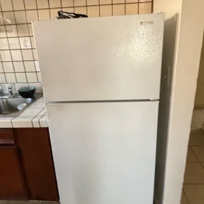 White top-freezer refrigerator positioned next to a kitchen counter and tiled backsplash.