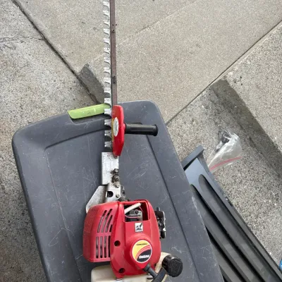 Red Shindaiwa professional gas-powered hedge trimmer resting on a plastic storage tote.