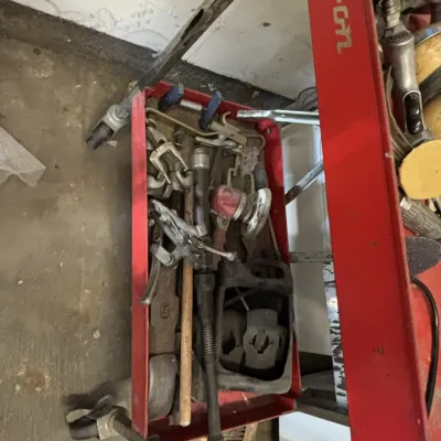 Red Snap-on rolling tool cart filled with assorted hand tools, air tools, and automotive hardware showing signs of wear.