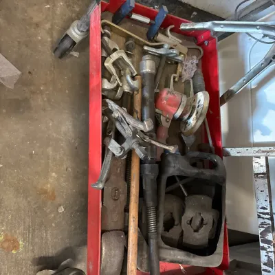 Red metal rolling utility cart filled with assorted hand tools, gear pullers, and automotive hardware showing signs of heavy use.