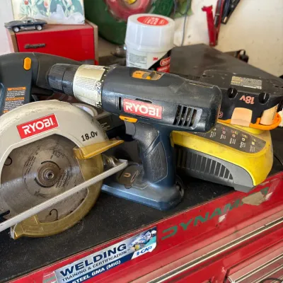 Ryobi 18.0V cordless power tool set, including a drill, circular saw, battery charger, and battery pack resting on a red tool chest.