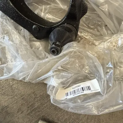 Black metal automotive suspension control arm with an integrated ball joint, packaged in clear plastic.