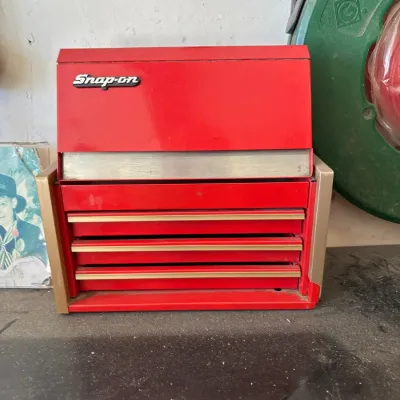 Vintage miniature red Snap-on branded metal tool chest featuring multiple drawers and a hinged top lid.