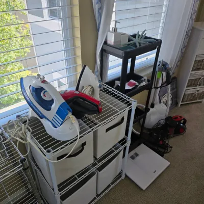 Sale Photo Thumbnail #91: Collection of modern household appliances, including multiple clothes irons, a upright fabric steamer, a digital bathroom scale, and wire shelving units.