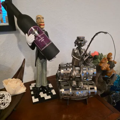 Sale Photo Thumbnail #12: Novelty wine accessories, including a butler figurine holding a large Vino Verona Merlot wine bottle gift set and a metal fisherman on stacked barrels wine rack.
