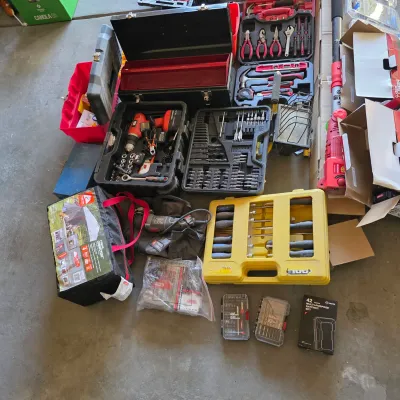 Sale Photo Thumbnail #138: Large assortment of power tools, hand tool sets, toolboxes, and outdoor gear displayed on a concrete floor.