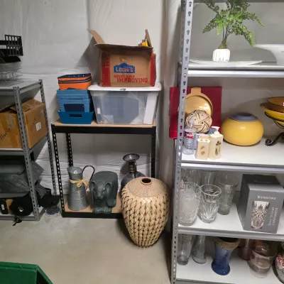 Sale Photo Thumbnail #54: Storage unit display featuring metal shelving units filled with home decor, glassware, a boxed Waterford crystal vase, woven urns, and storage containers.