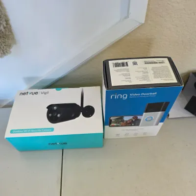 Sale Photo Thumbnail #153: Two boxed home security electronics, including a Netvue Vigil outdoor Wi-Fi security camera and a Ring Video Doorbell.